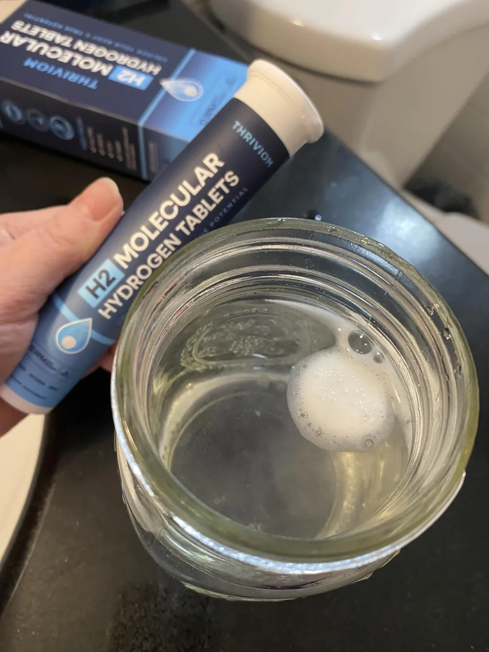 Reviewer holding a Thriviom tablet tube beside a glass of dissolving water