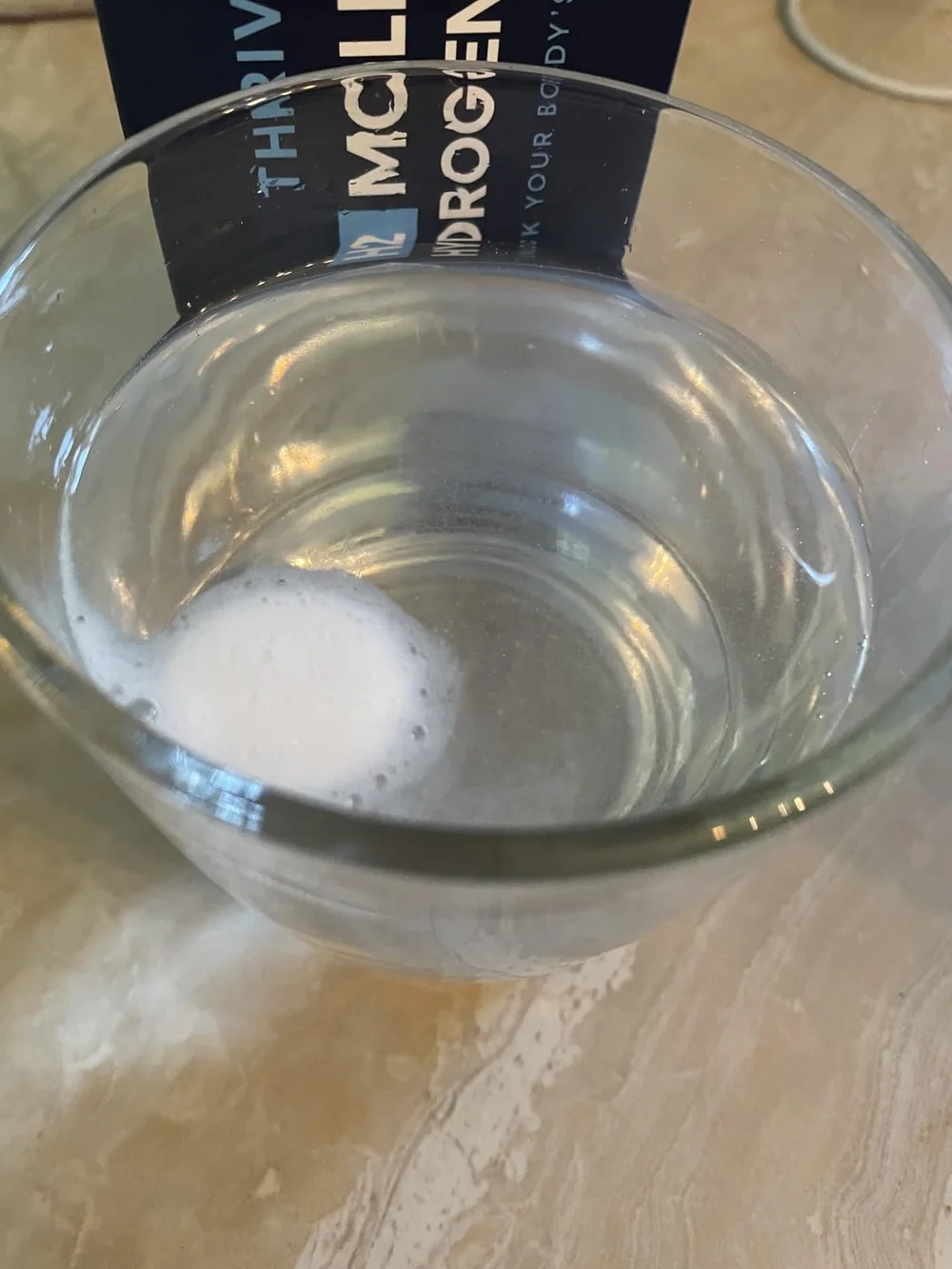 Hydrogen tablet fizzing and dissolving in a glass of water with the tube visible behind it