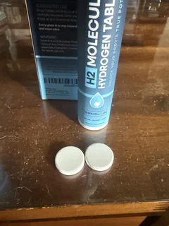 Thriviom H2 Molecular Hydrogen Tablets tube with two tablets set beside it on a wooden table