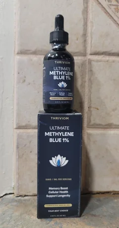 Thriviom Ultimate Methylene Blue 1% bottle standing in front of its box on a stone surface