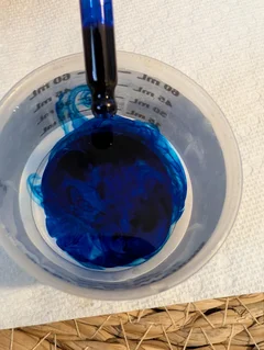 Methylene Blue solution swirling into a dose cup of water from the dropper