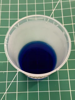 Methylene Blue dissolved in a small cup of water on a wooden cutting board